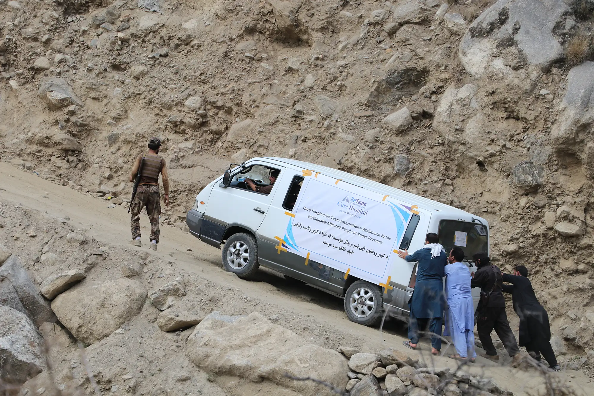 Be Team International Cure Hospital team pushing a medical vehicle up a steep mountain road in Afghanistan during a crisis response trip