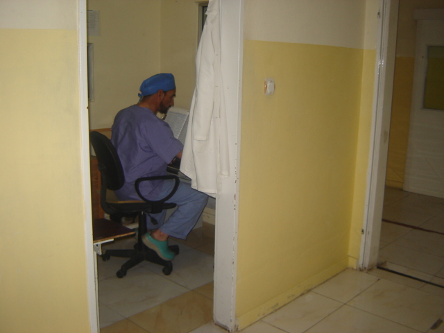 Be Team International Cure Hospital surgeon completing documentation at his computer in Kabul, Afghanistan, still in surgical scrubs
