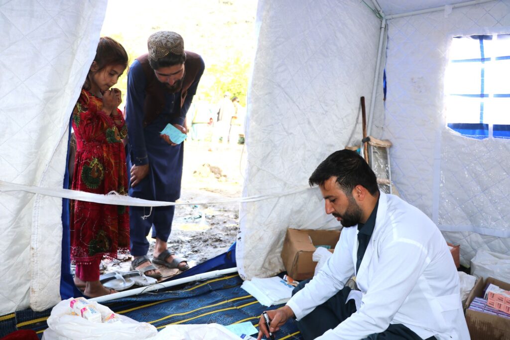 Be Team International Cure Hospital team member dispensing medicine to a father and young daughter inside a temporary tent during a medical camp in Afghanistan