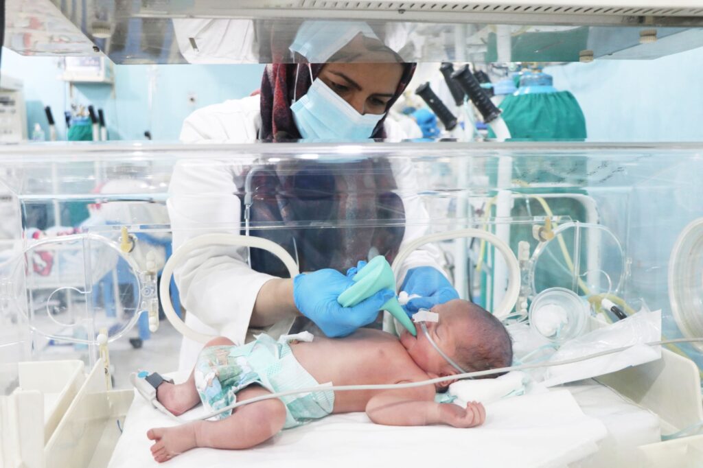 Nurse patiently feeding a newborn baby in an NICU crib at Be Team International's Cure Hospital in Kabul, Afghanistan