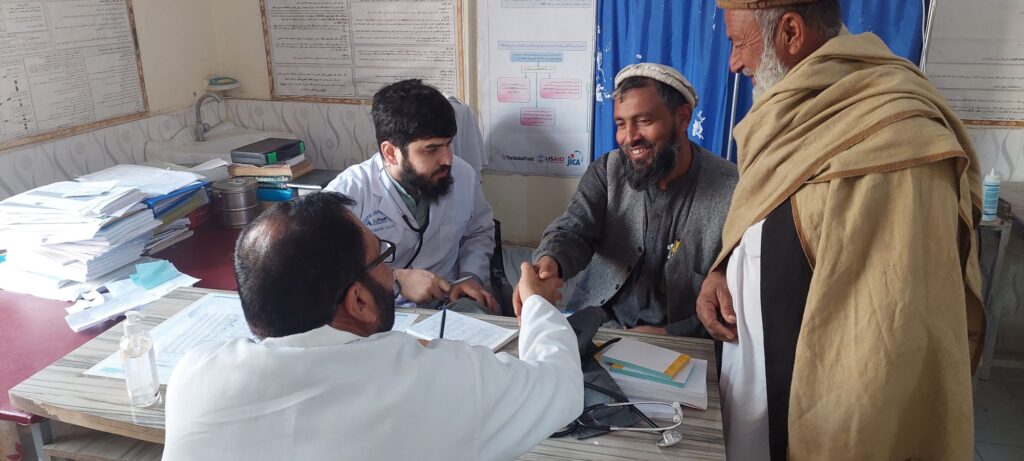 Afghan man warmly shaking hands with a Be Team International Cure Hospital colleague during patient intake at a medical camp in Laghman, Afghanistan