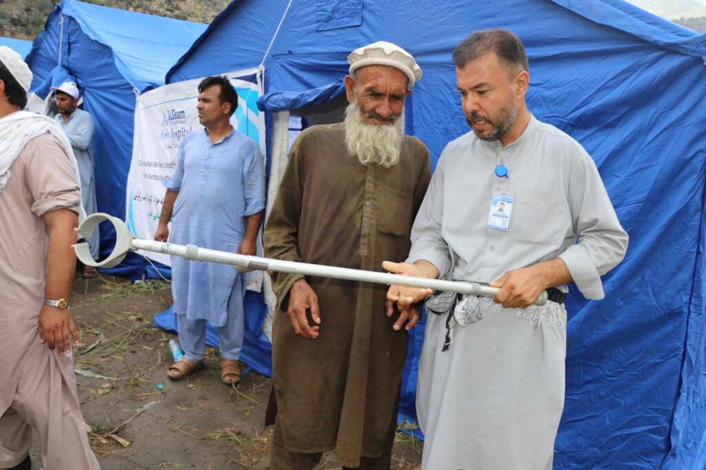 Be Team International Cure Hospital team member demonstrating crutch use to an elderly smiling man during a medical camp in Afghanistan